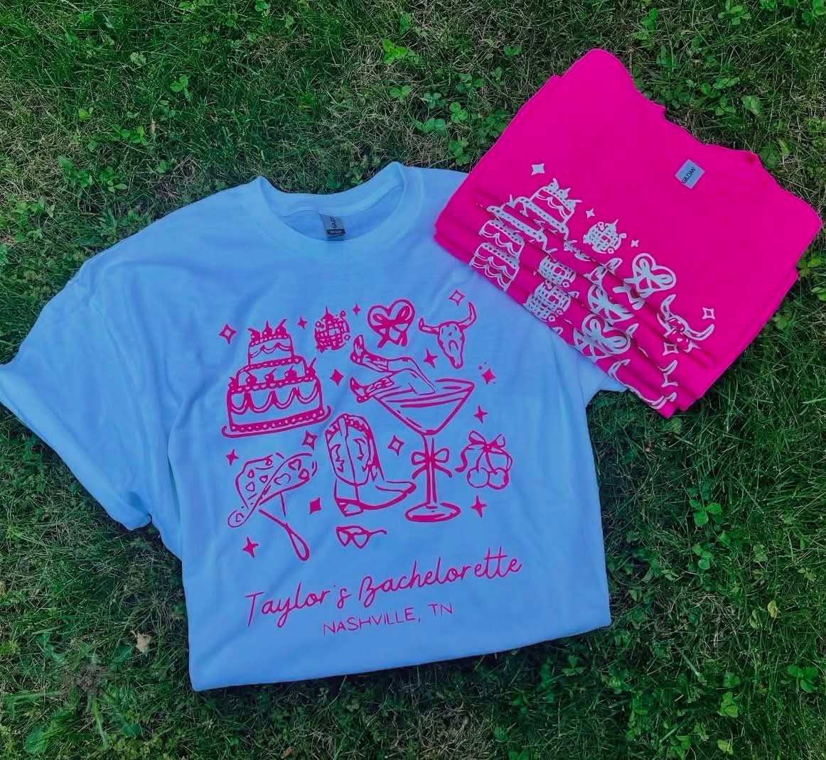 Light blue tee with a pink illustrated bachelorette design reading Taylor's Bachelorette, Nashville TN, folded beside a matching pink sweatshirt