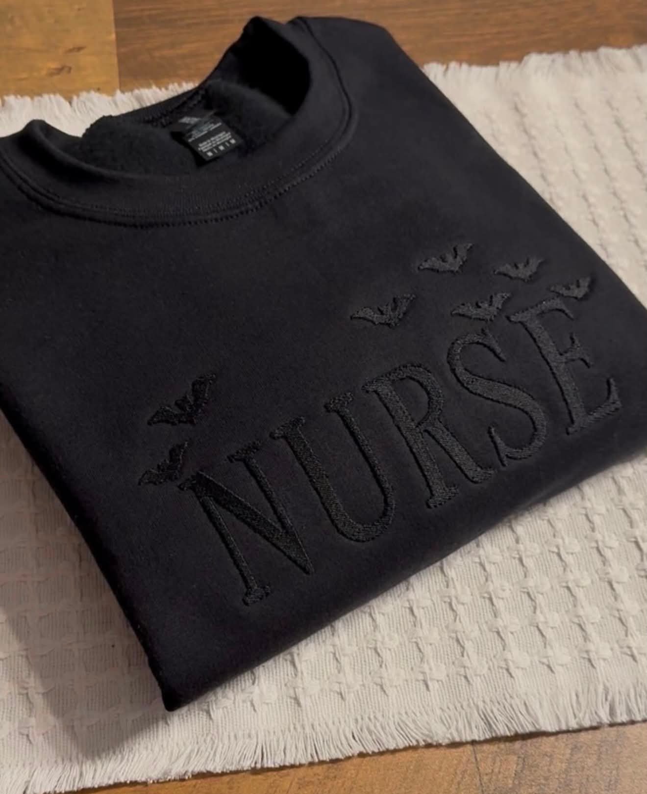 Black crewneck with tonal black embroidery reading Nurse surrounded by bats