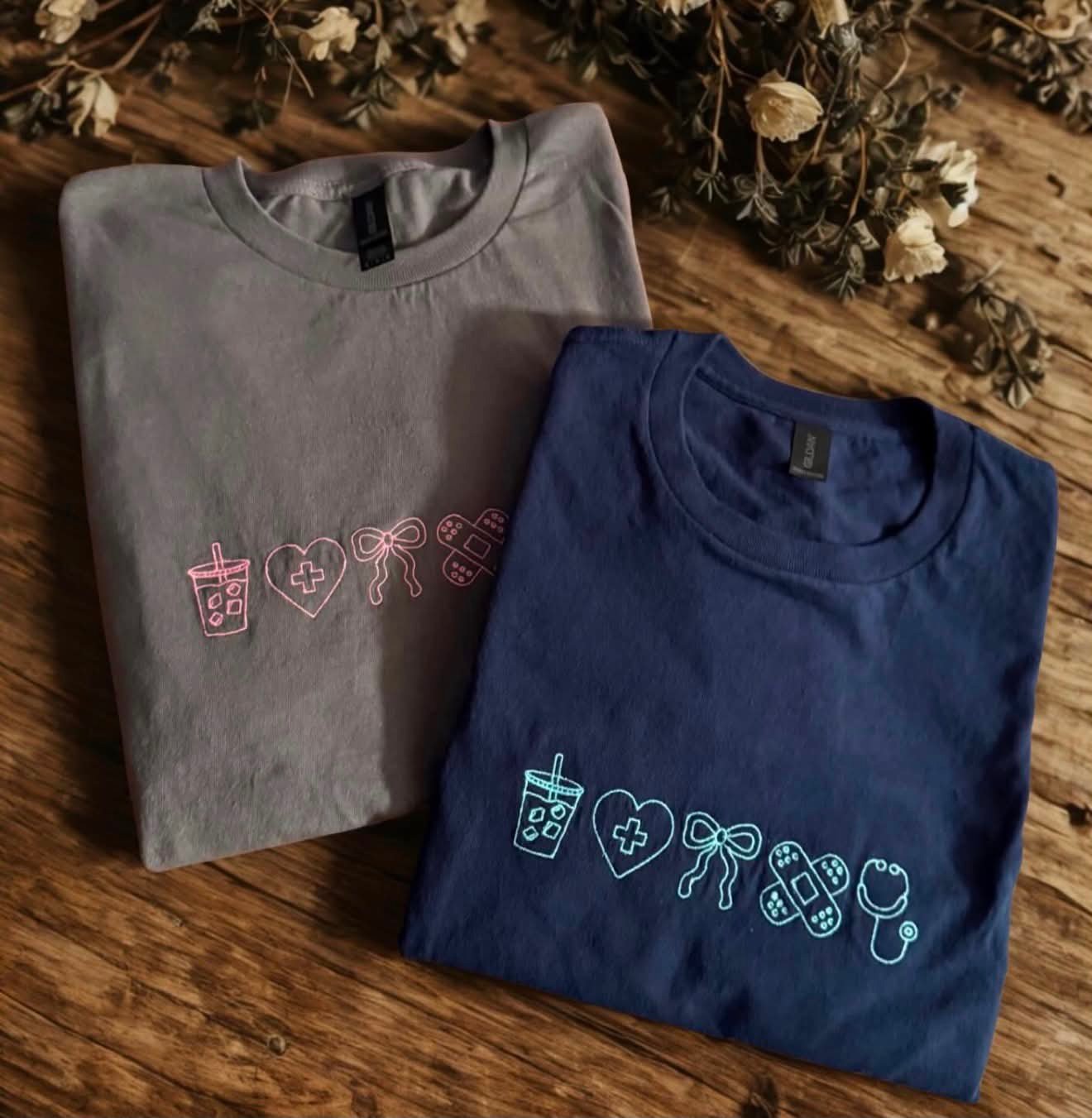 Grey and navy tees embroidered with a row of icons including an iced coffee, heart, bow, bandage and stethoscope