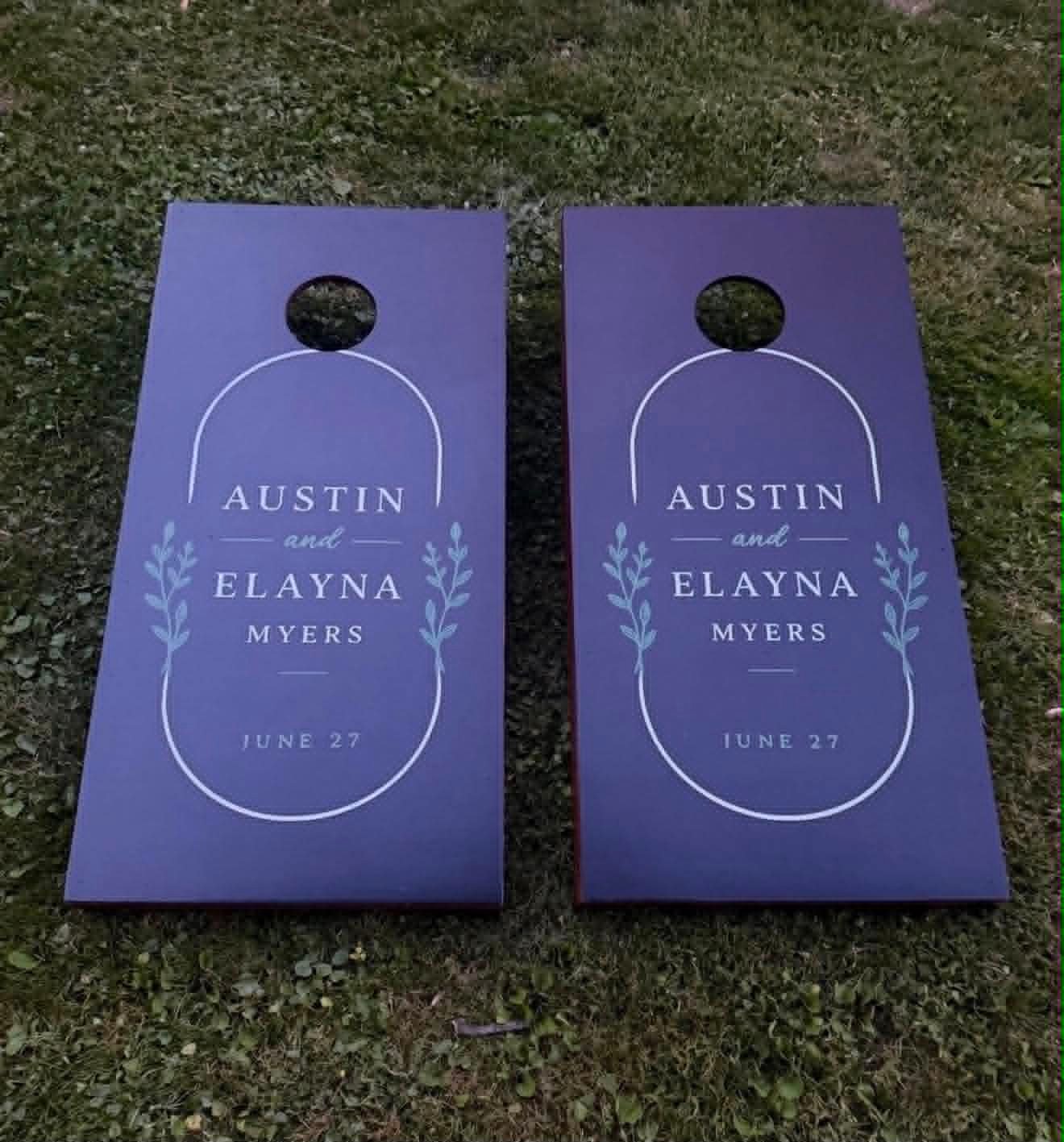 Navy blue wedding cornhole board set reading Austin and Elayna Myers, June 27, with an arched wreath design