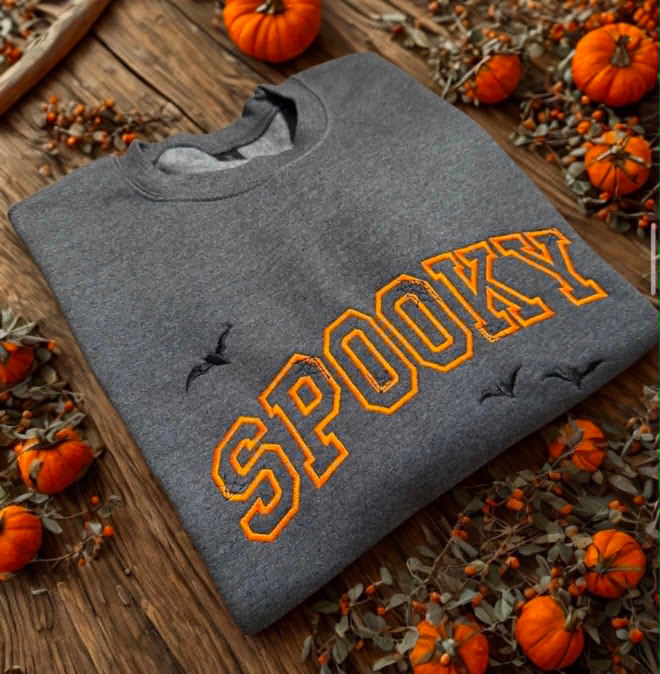 Heather grey Gildan crewneck embroidered with Spooky in orange lettering and bats