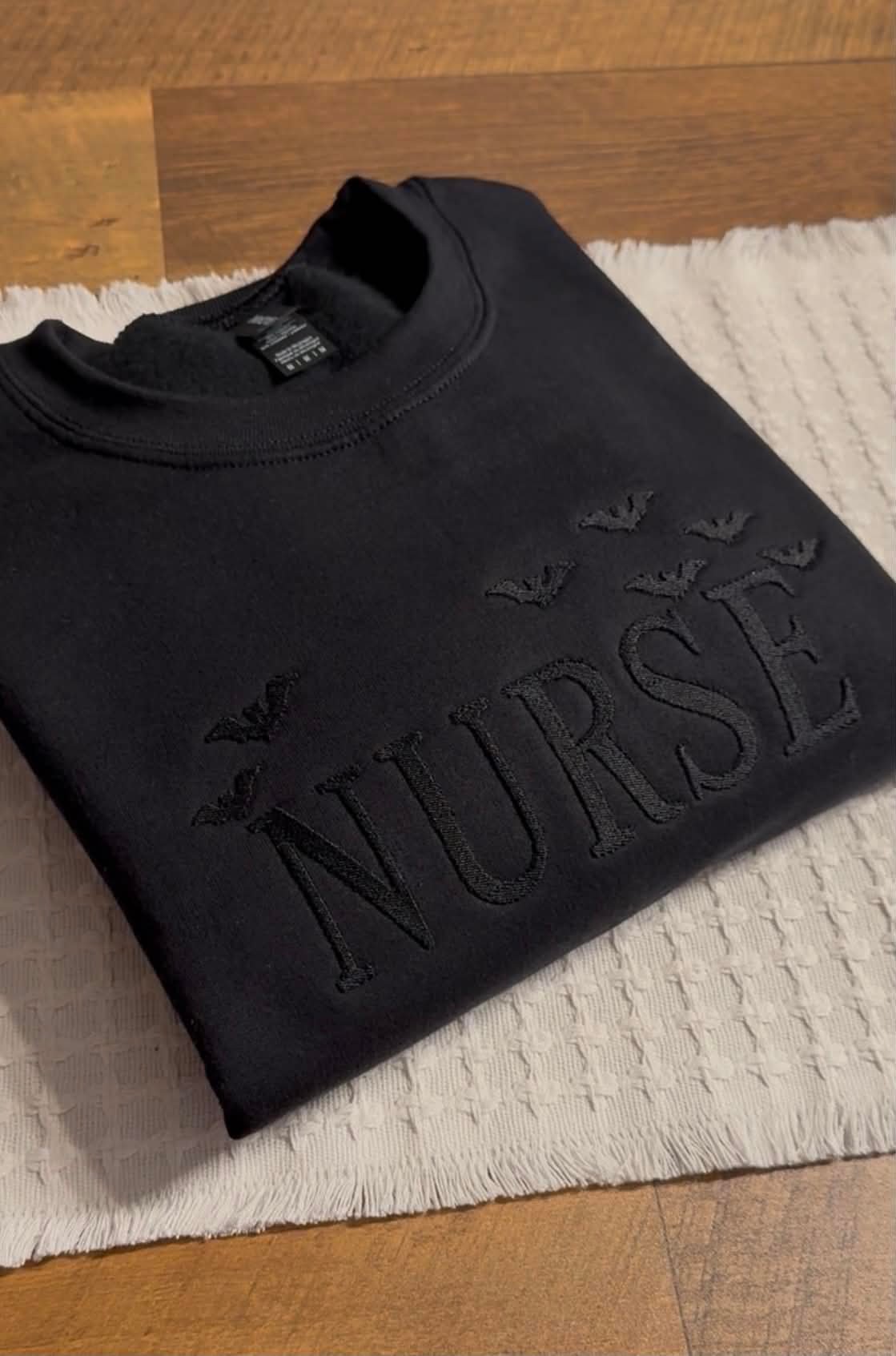 Black Gildan crewneck with tonal black embroidery reading Nurse surrounded by bats