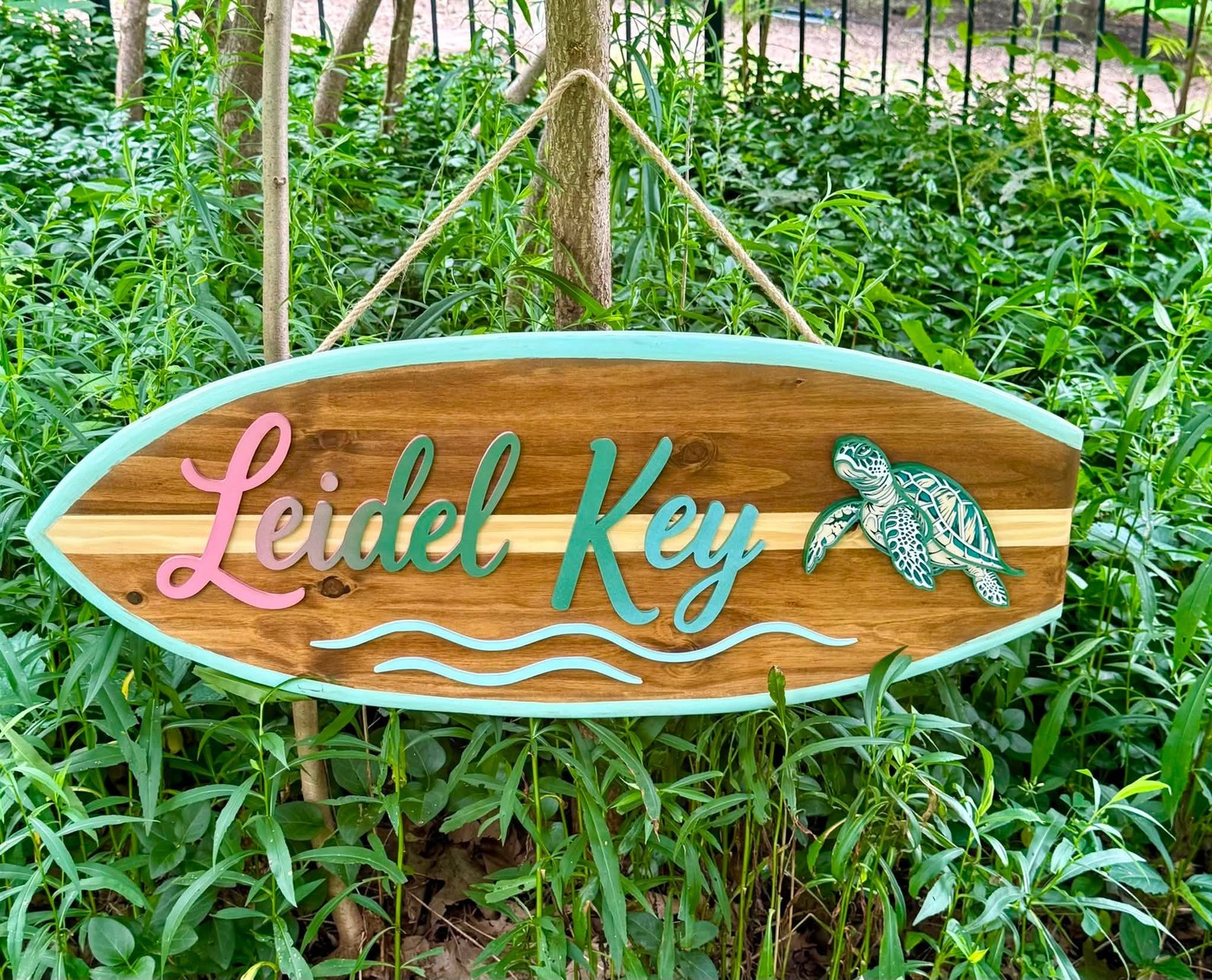 Hand-painted surfboard-shaped welcome sign reading Leidel Key with a sea turtle